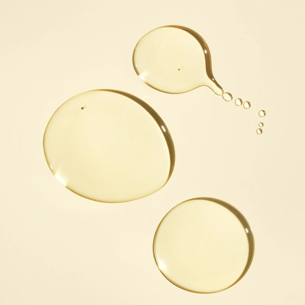 Close-up of three droplets of yellow liquid on a beige background