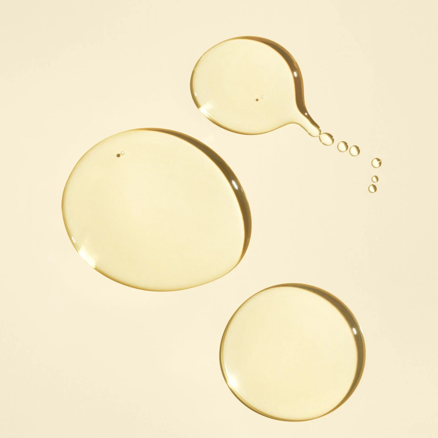Close-up of three droplets of yellow liquid on a beige background