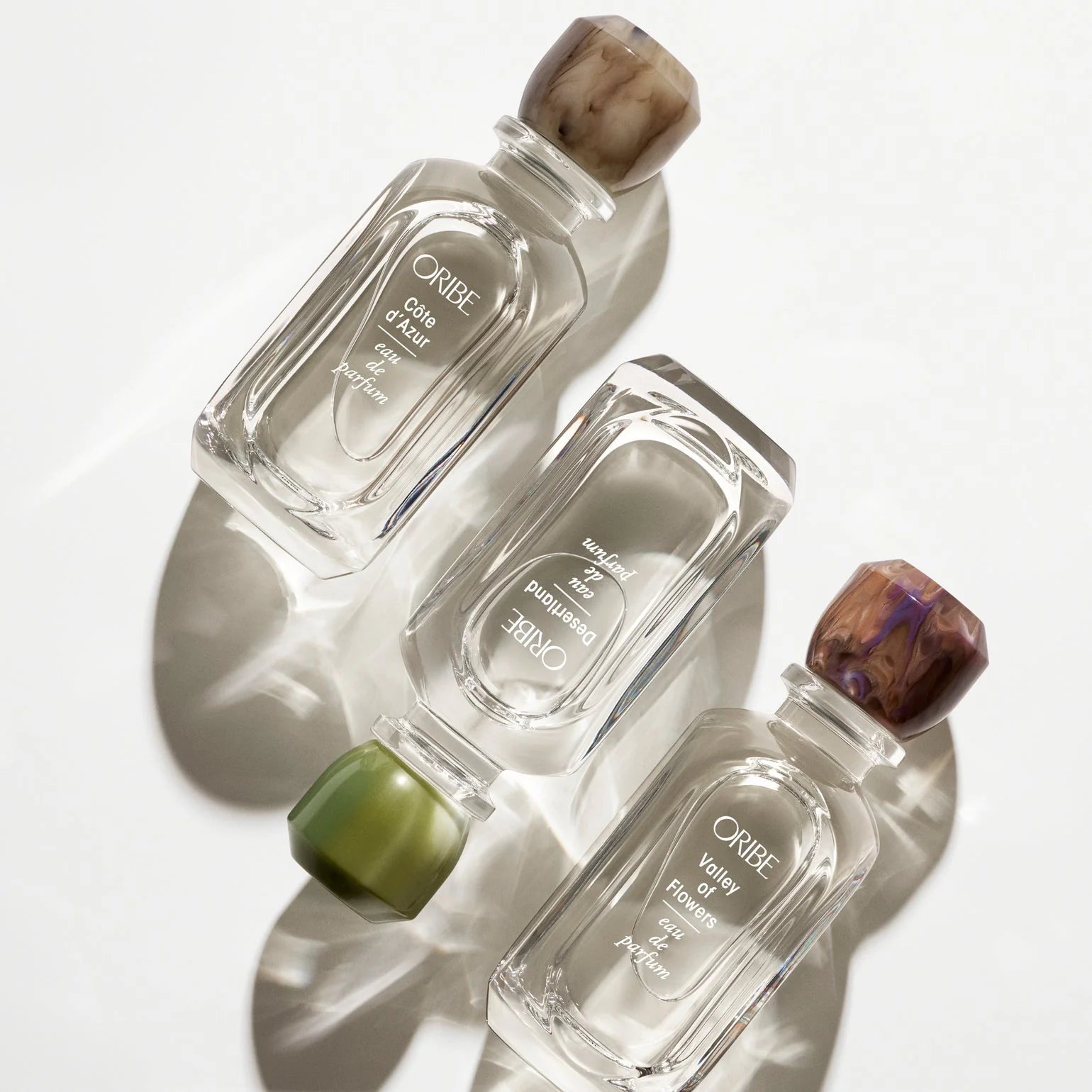 Three Oribe perfume bottles with natural stone caps on a white background