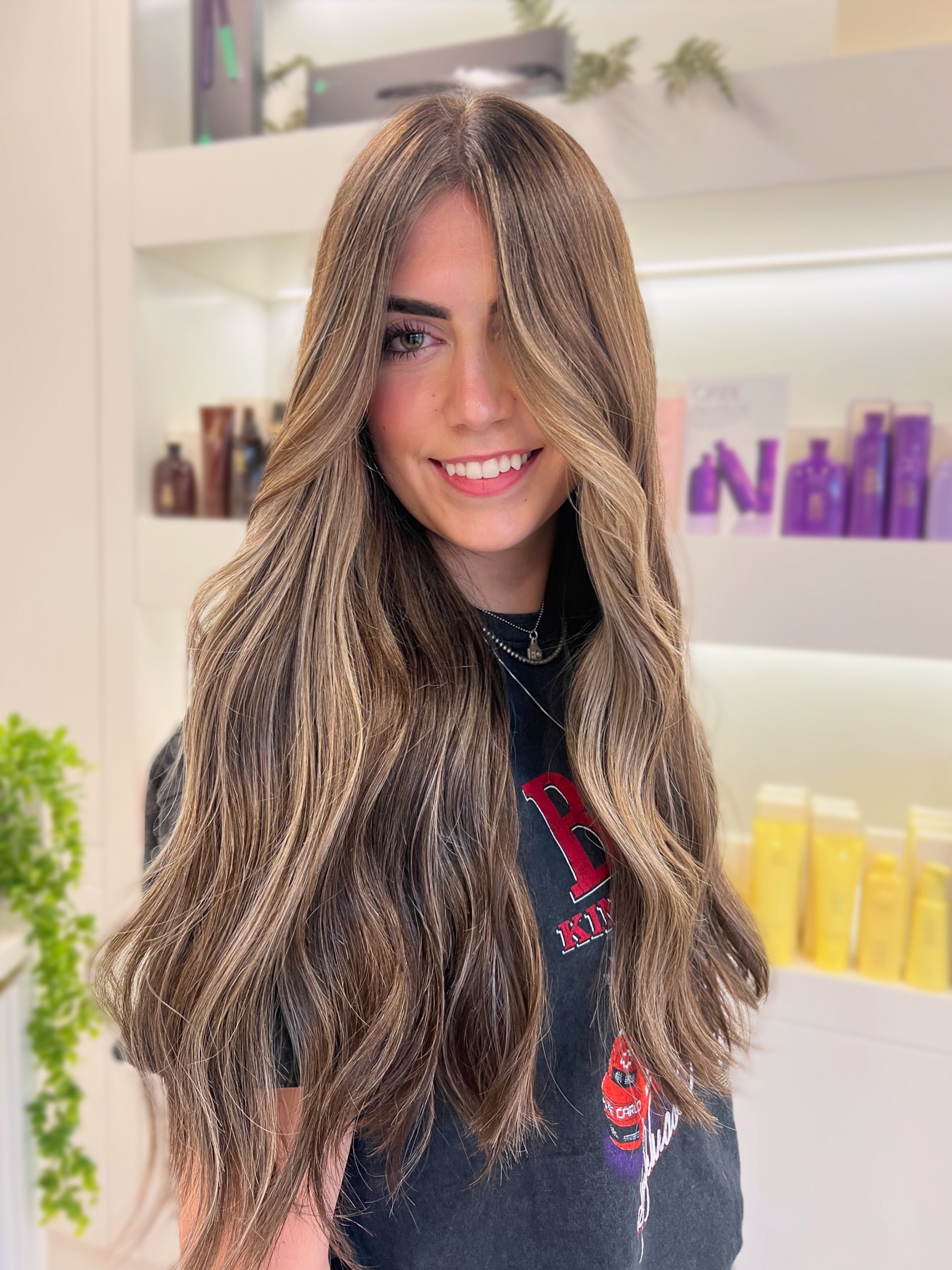 Woman with long, wavy hair in a salon setting with products in the background