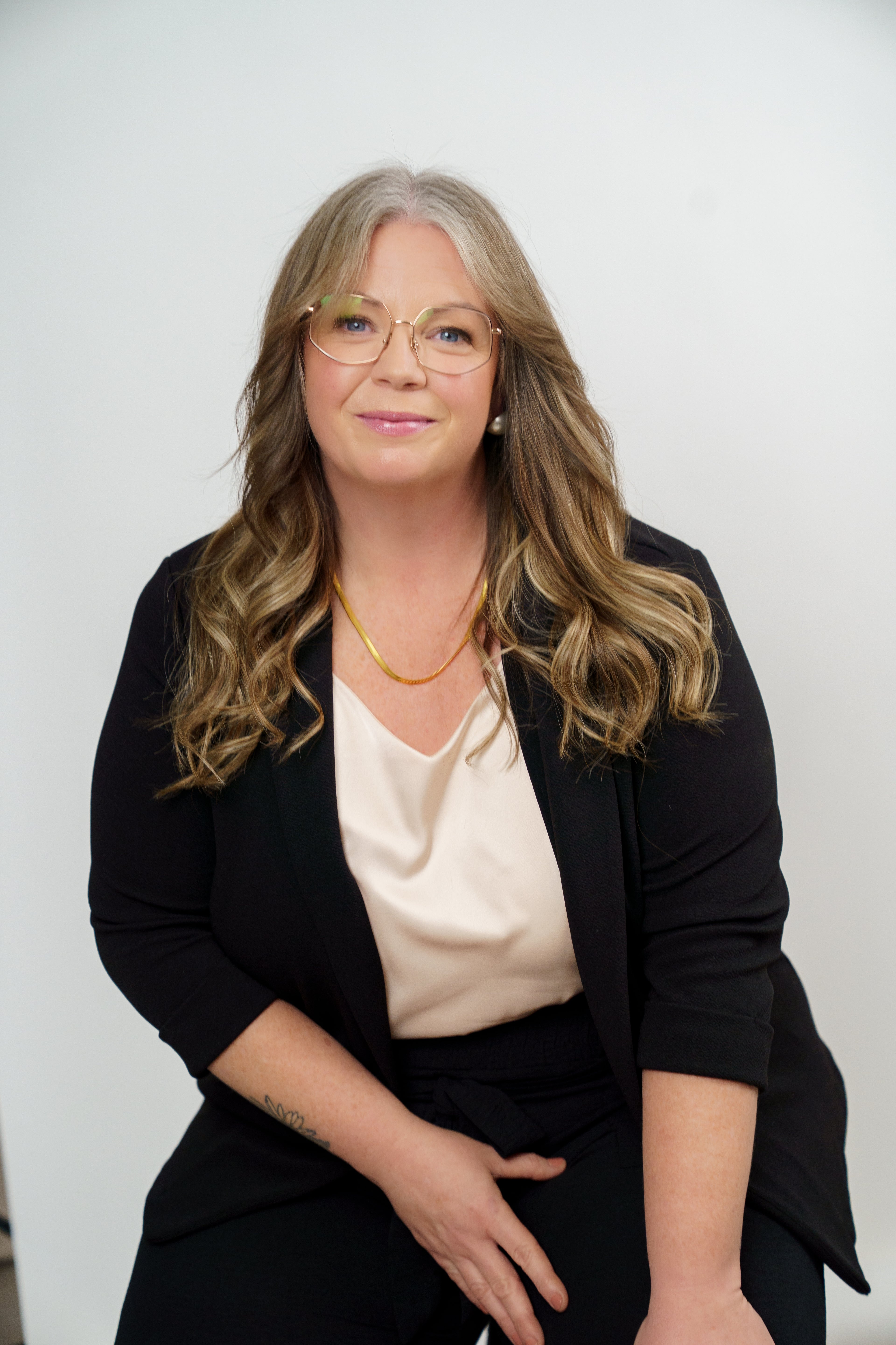 Woman wearing glasses and a black blazer over a white shirt against a plain background